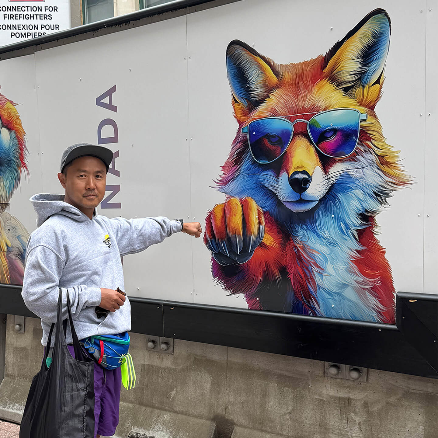 Posing for a photo in front of a billobard with cartoon fox giving a fist-bump.